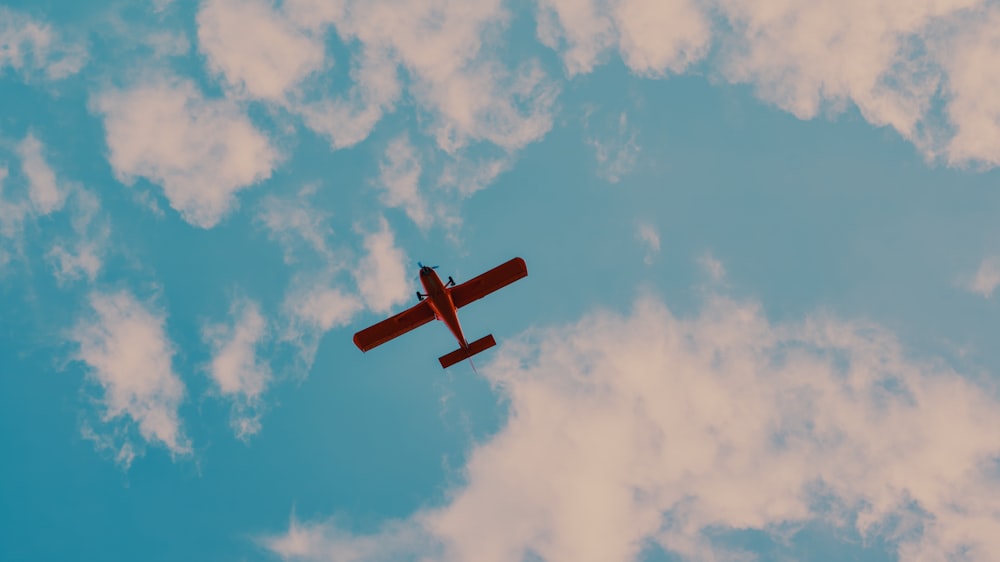 a red airplane flying through a cloudy blue sky