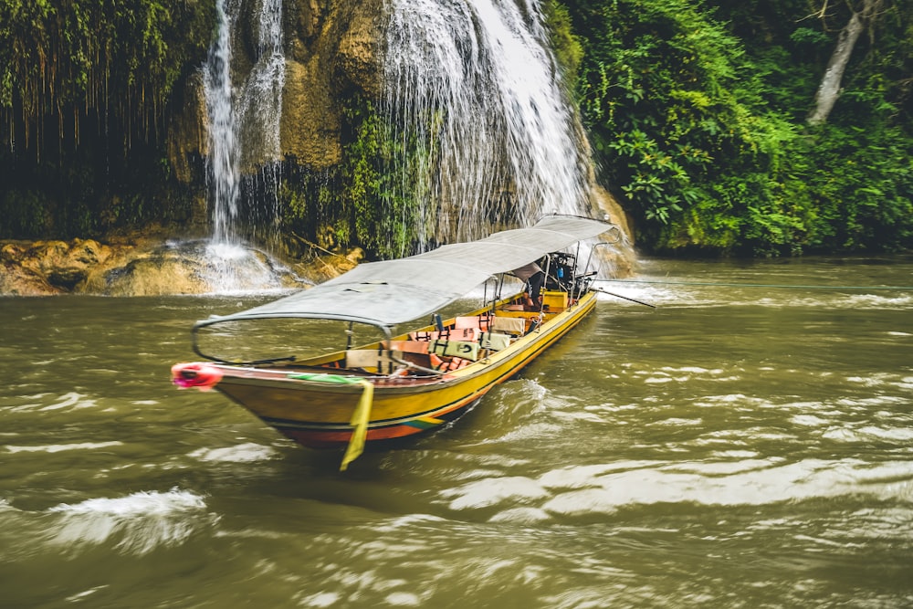 a yellow boat with passengers in front of a waterfall