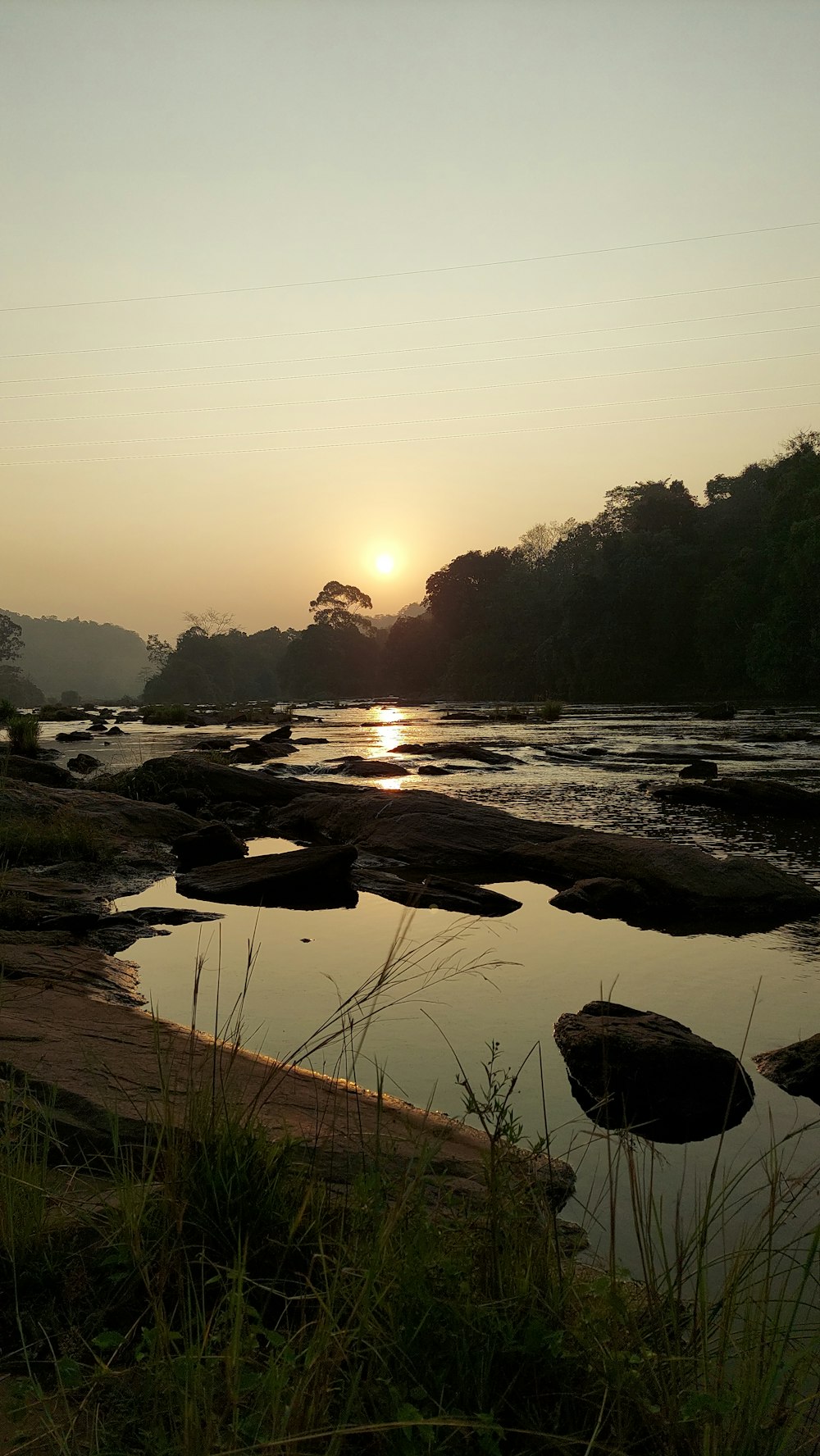 the sun is setting over a river with rocks