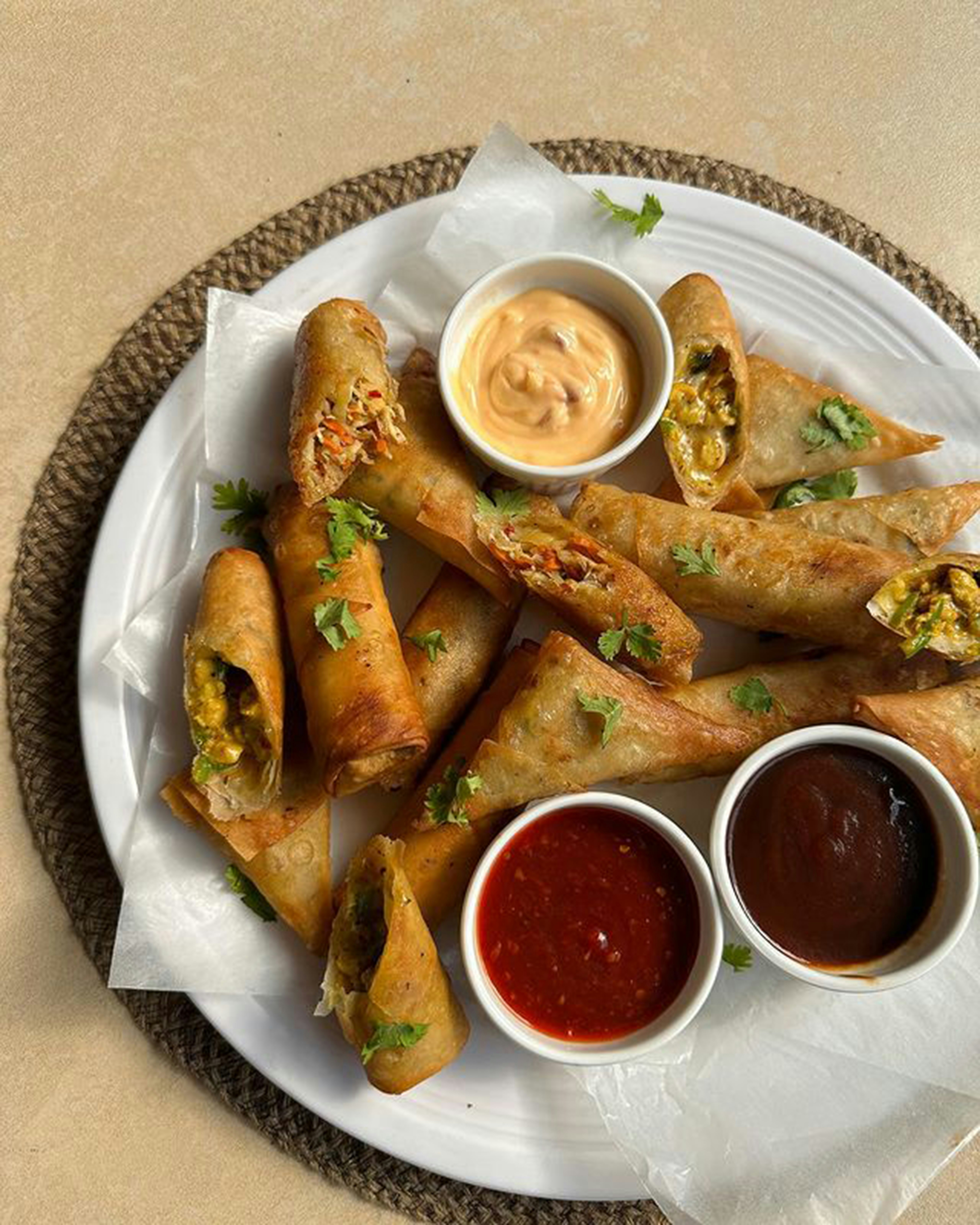 Golden crispy samosas and spring rolls on white platter, studio light