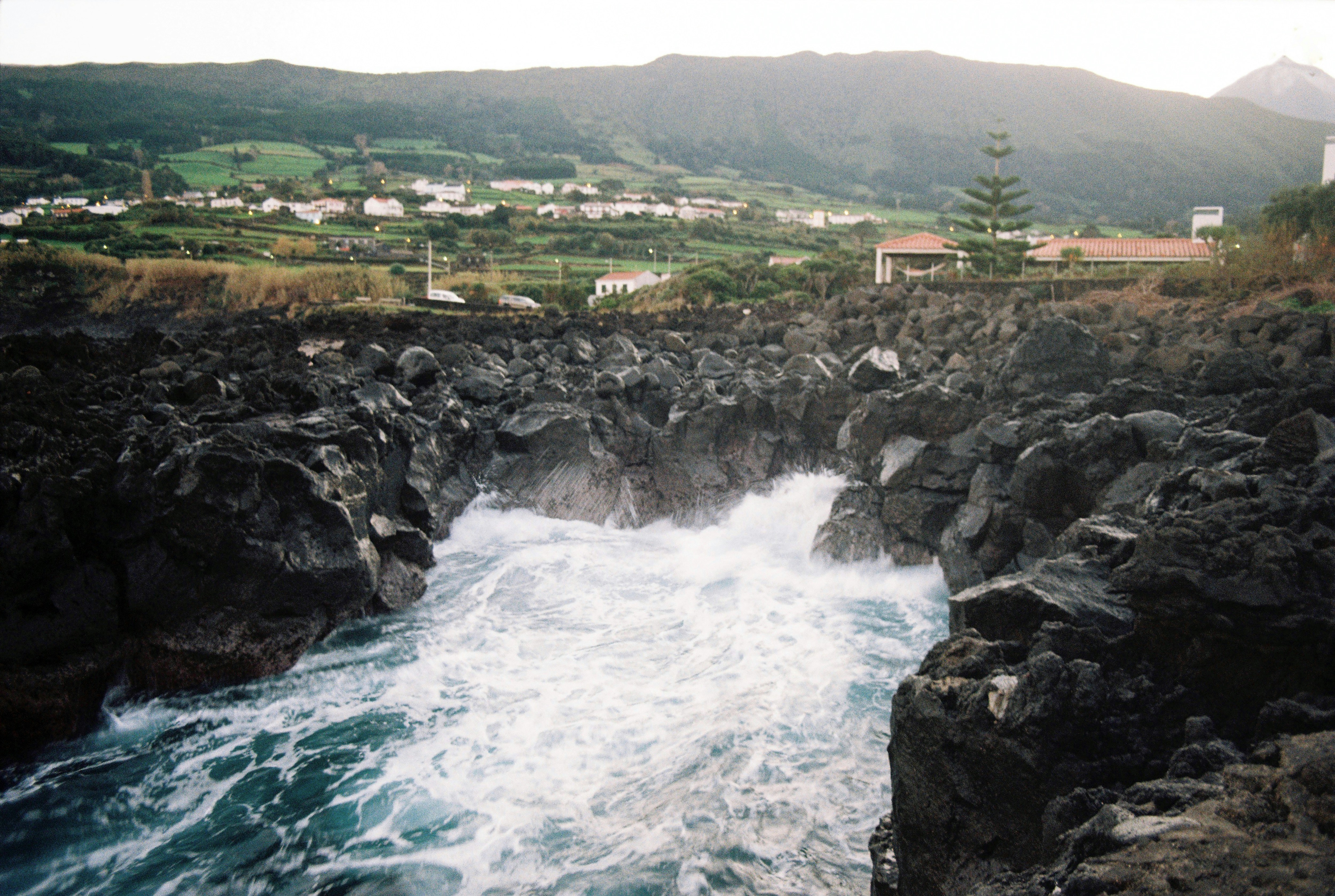 a large body of water near a rocky shore, The sea crashing against the rocks on Pico Island, Azores on film.