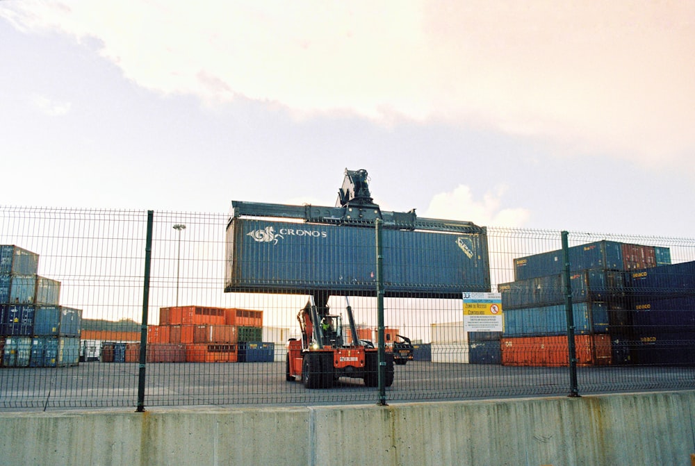 Un carrello elevatore sta spostando un grande contenitore dietro una recinzione