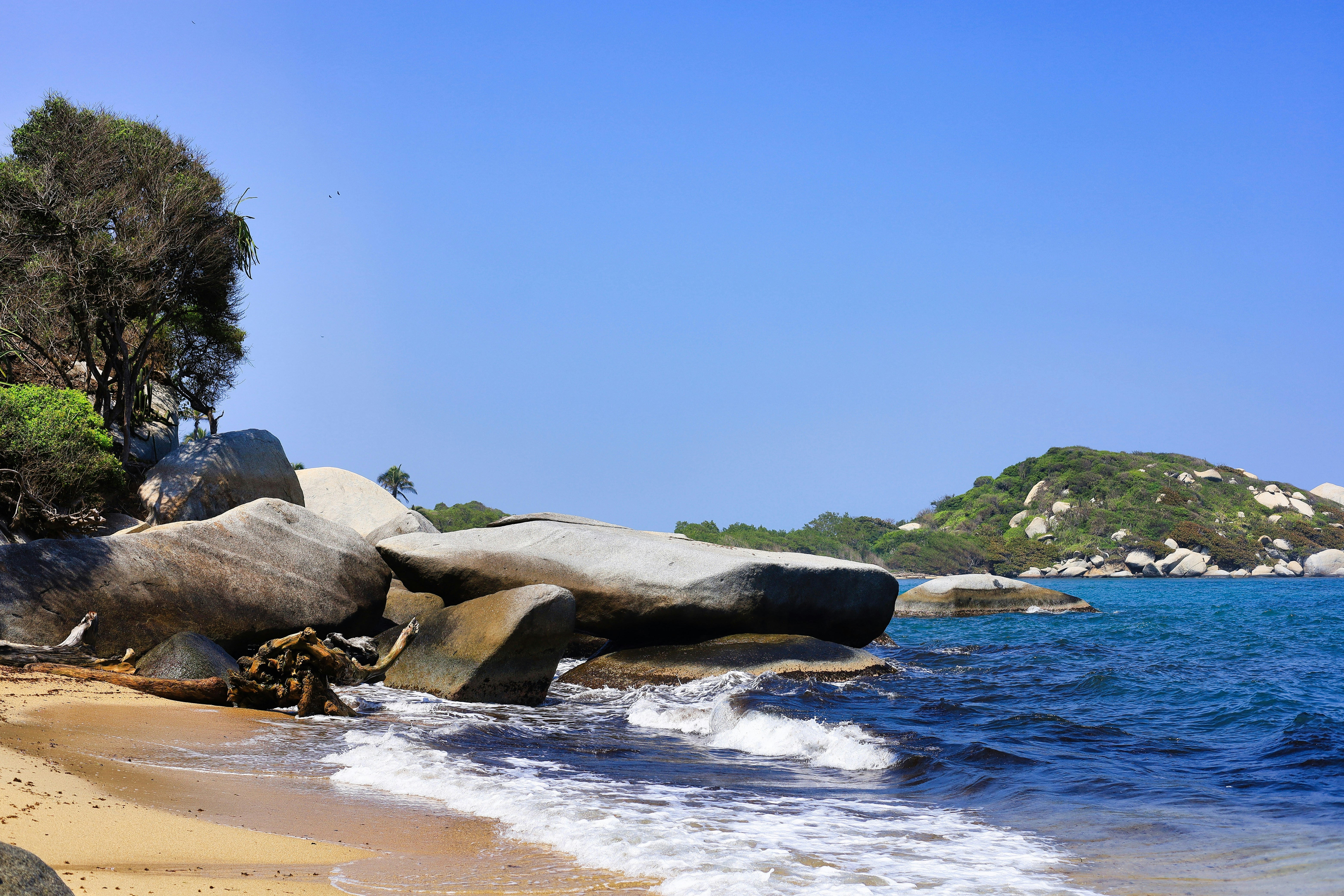 a sandy beach with large rocks and water, 