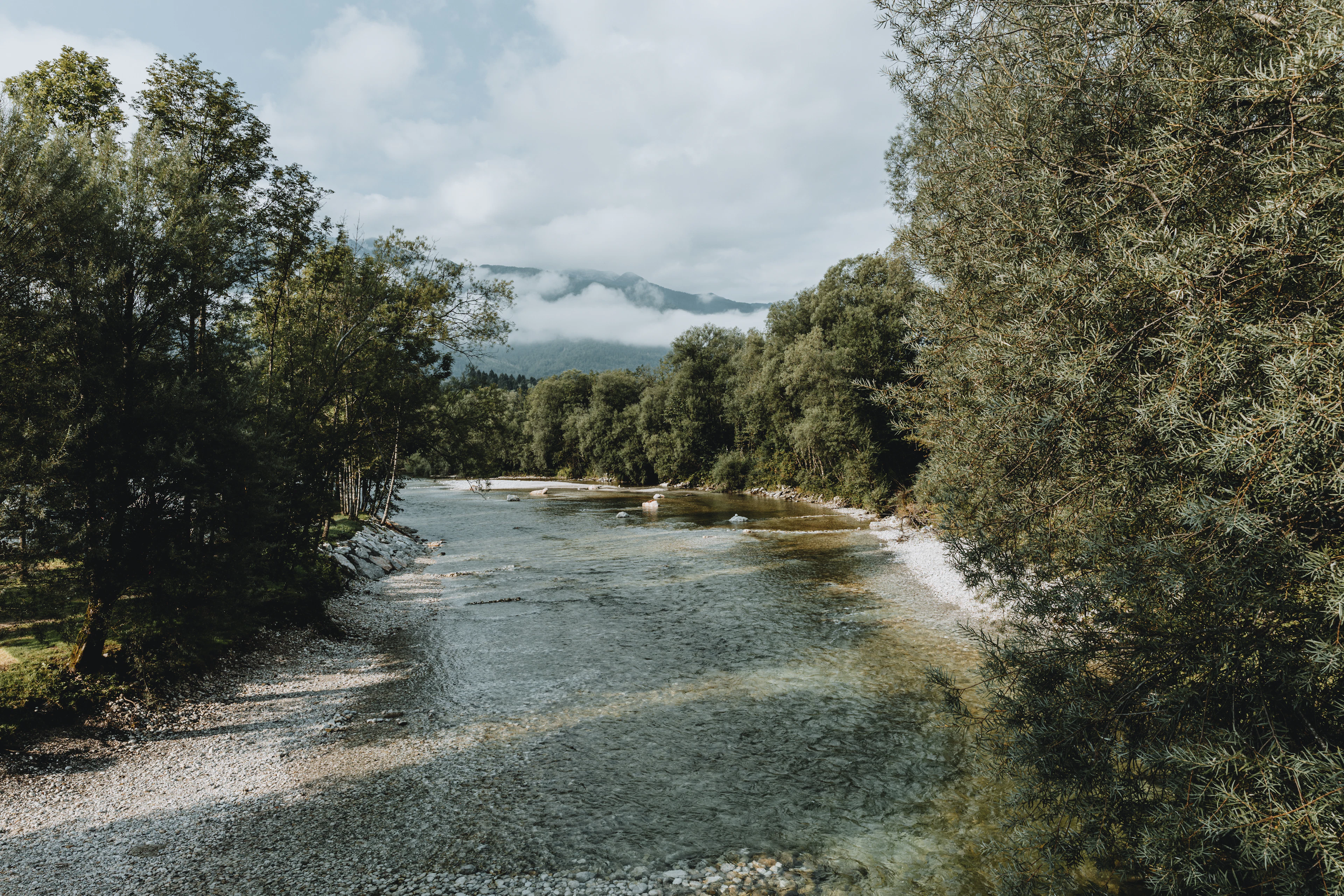 Morning light on the shallow, clear Soča river, with low cloud on the mountains beyond, Slovenia