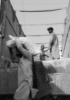 a black and white photo of two men loading a truck