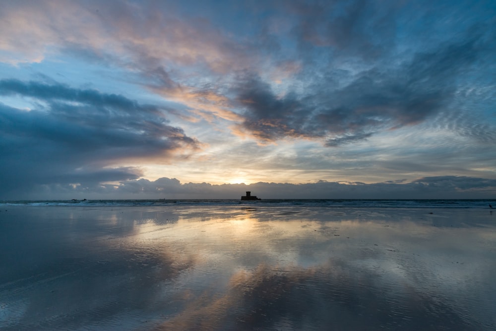 the sun is setting over the water on the beach