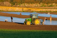 a tractor is plowing a field with people nearby
