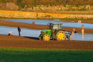 a tractor is plowing a field with people nearby