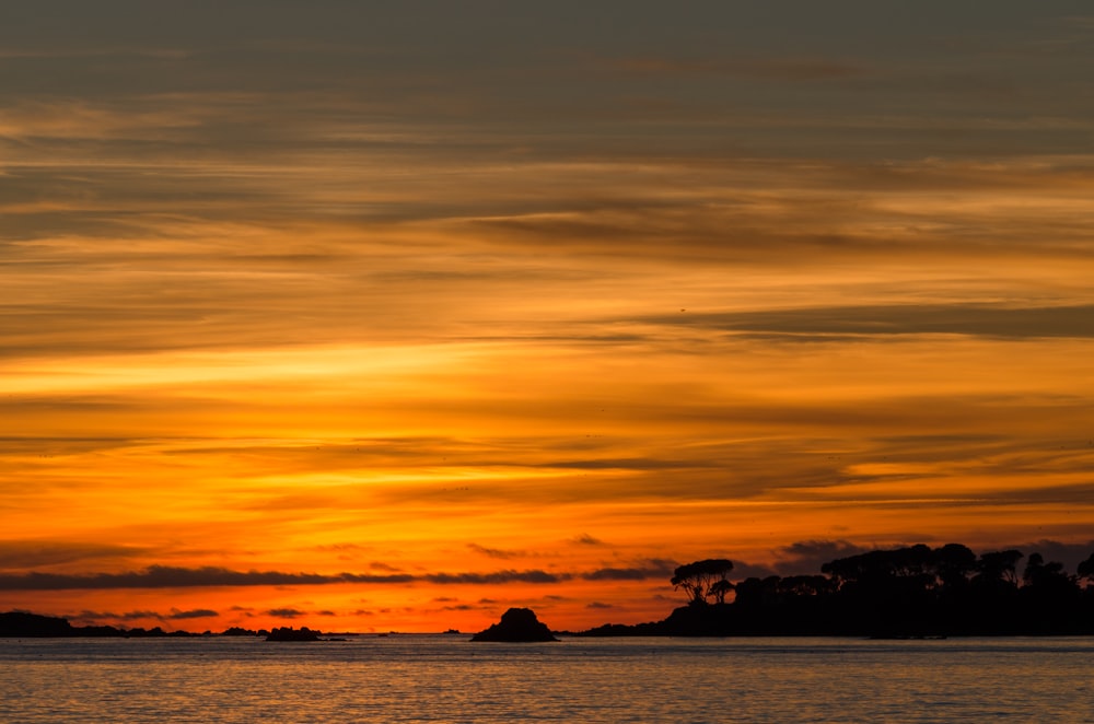 ein Sonnenuntergang über einem Gewässer mit einer kleinen Insel in der Ferne