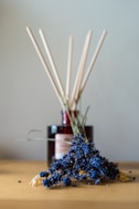 a wooden table topped with a bottle of liquid and sticks of reeds