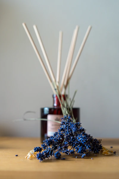 a wooden table topped with a bottle of liquid and sticks of reeds