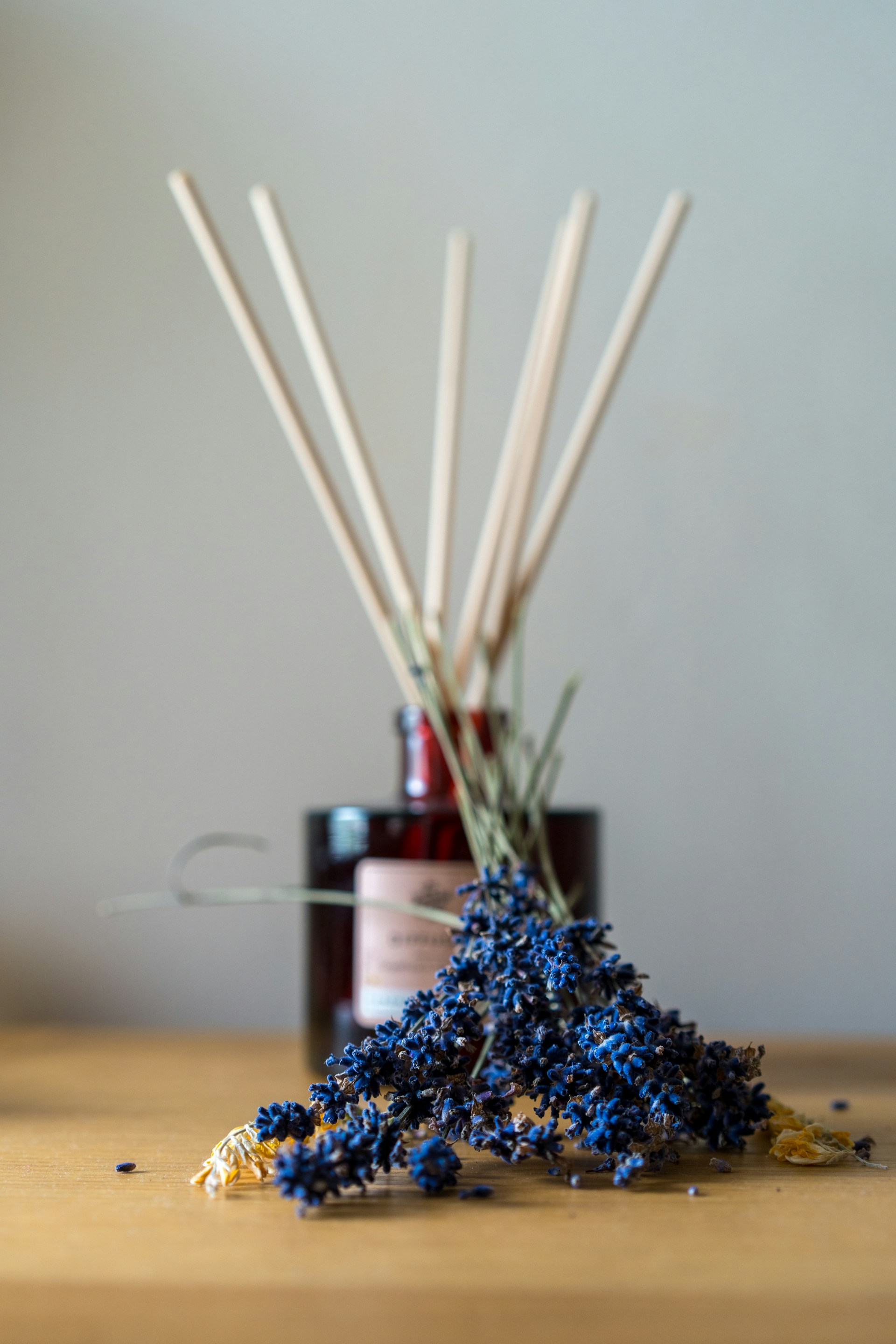 a wooden table topped with a bottle of liquid and sticks of reeds