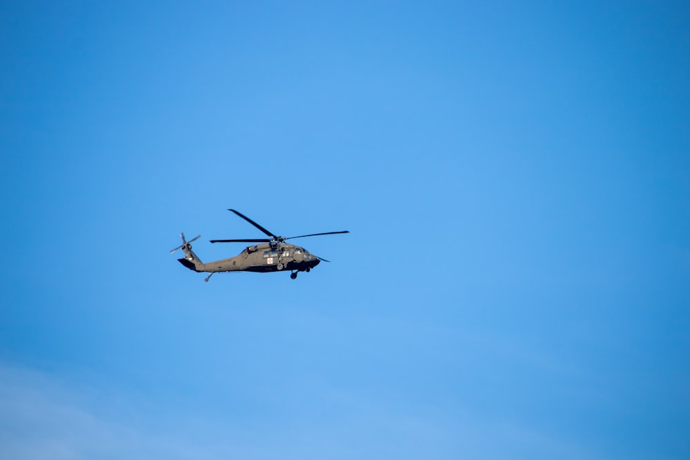 a military helicopter flying through a blue sky