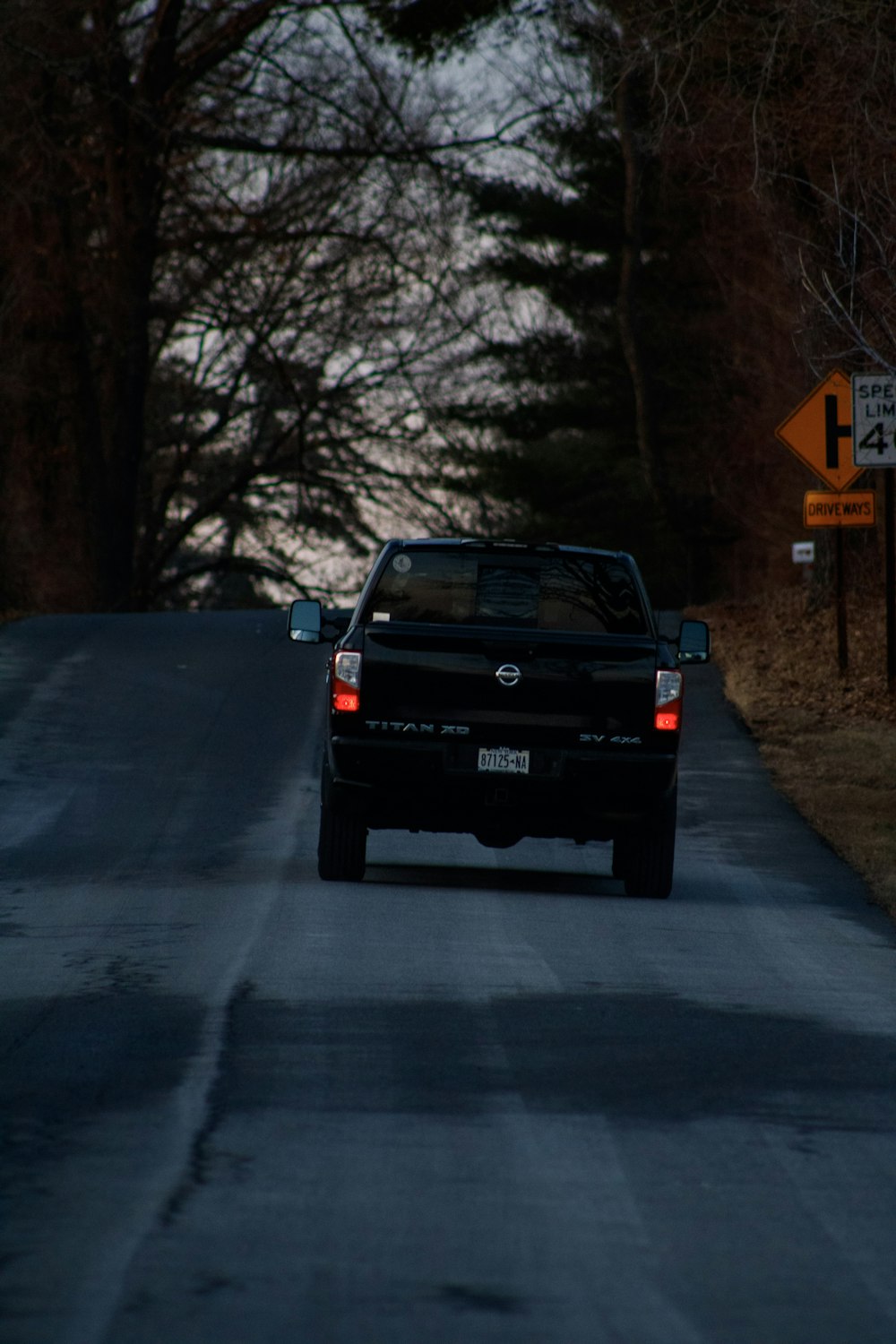 a black truck driving down a road next to a forest