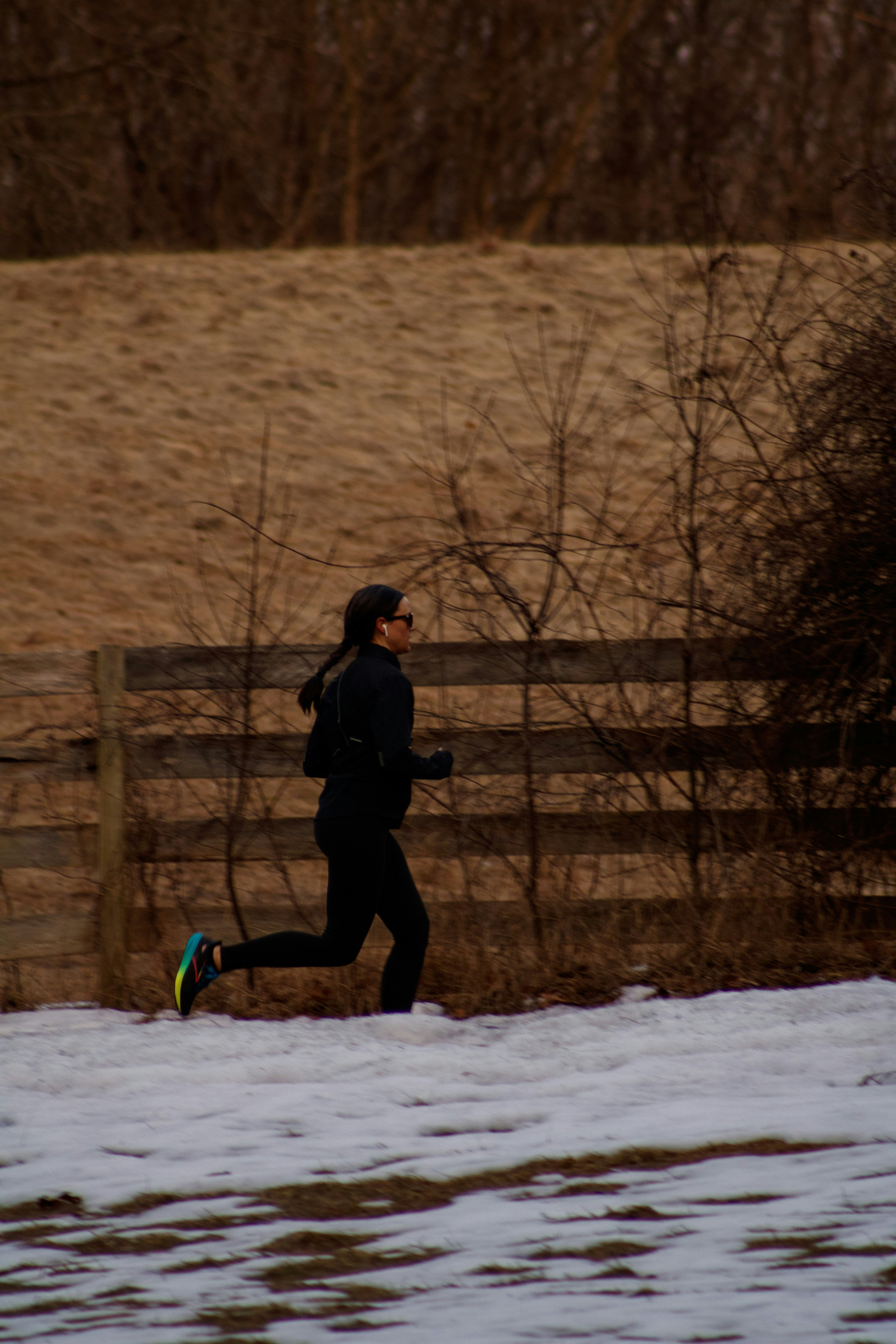Runner in black layers, gloves and sunglasses jogging past a wooden fence in late-autumn light