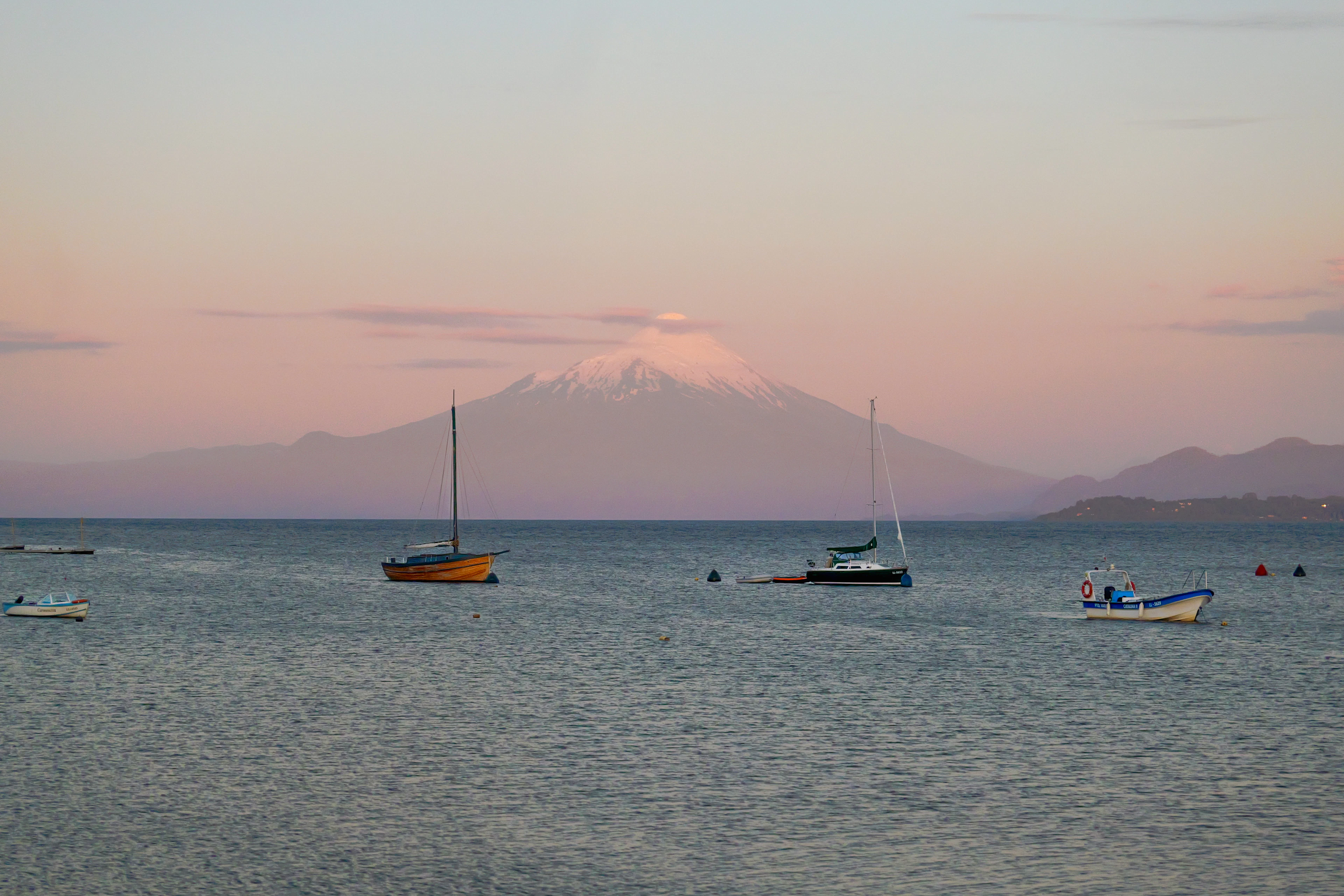 Osorno volcano in a pink dusk above Lake Llanquihue, with small boats at anchor, Puerto Varas, Chile