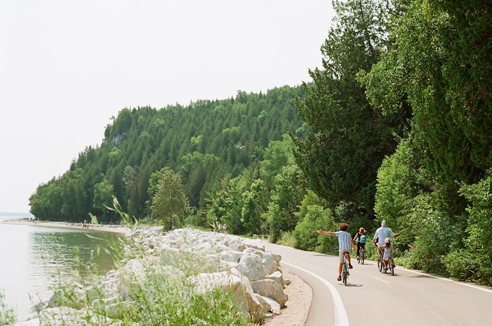 a group of people riding bikes down a road next to a lake