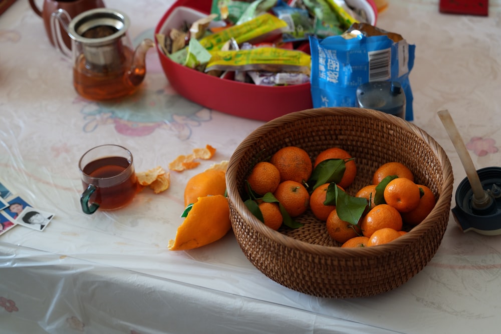 a basket of oranges sitting on a table next to a cup of tea