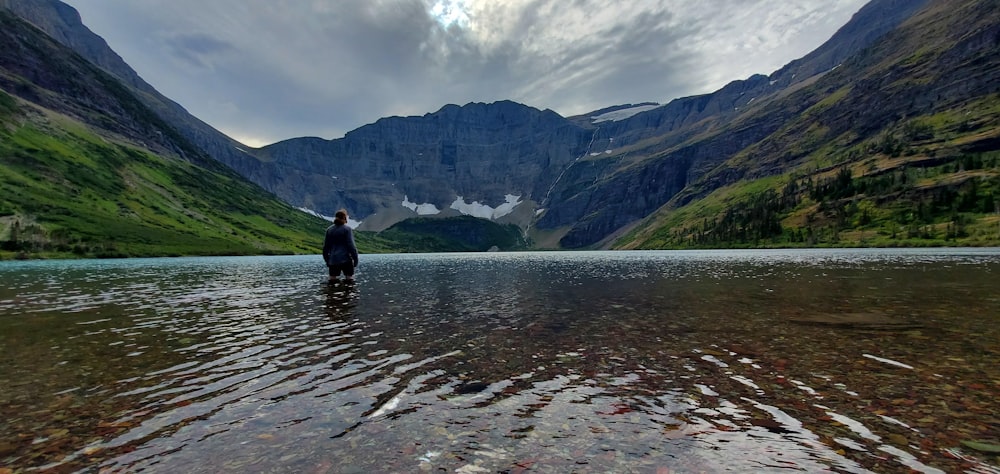 a man standing in a lake surrounded by mountains