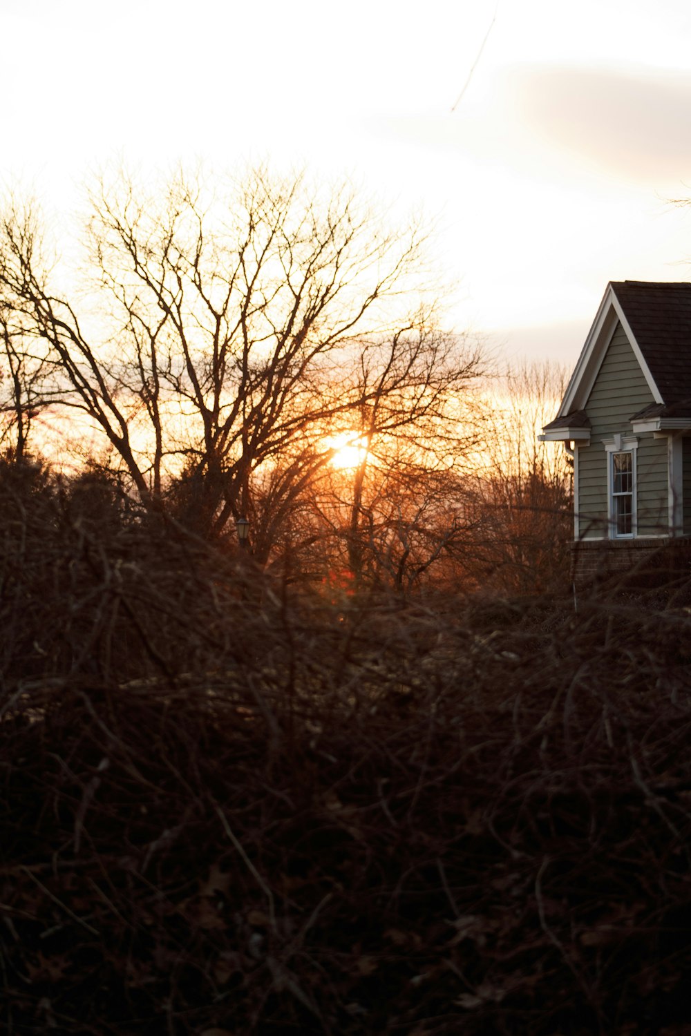 the sun is setting behind a house in a field