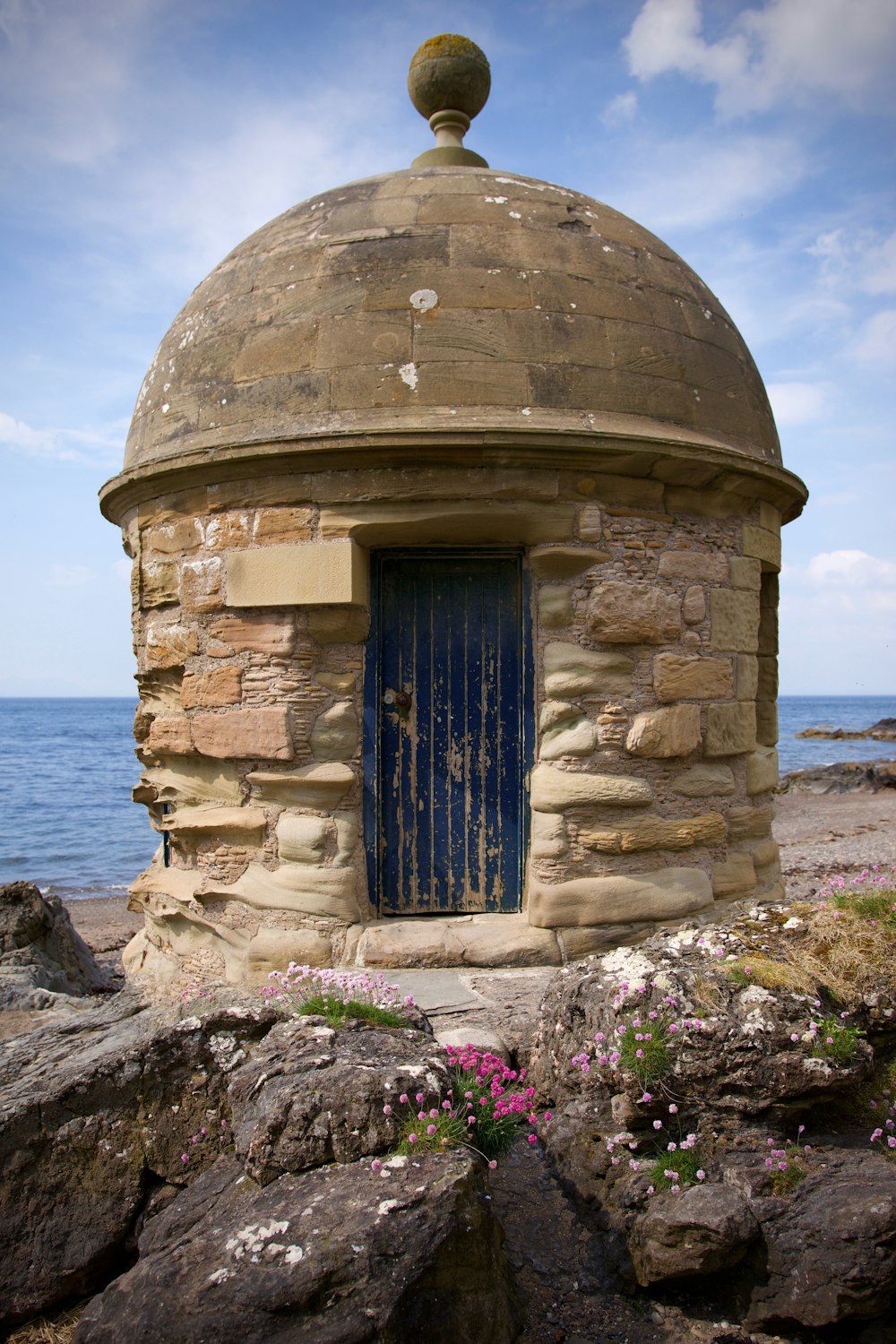 a stone structure with a blue door on a rocky shore