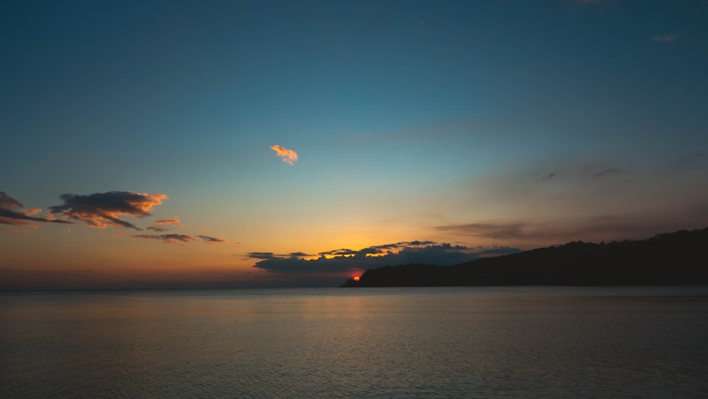 the sun is setting over the ocean with a mountain in the distance