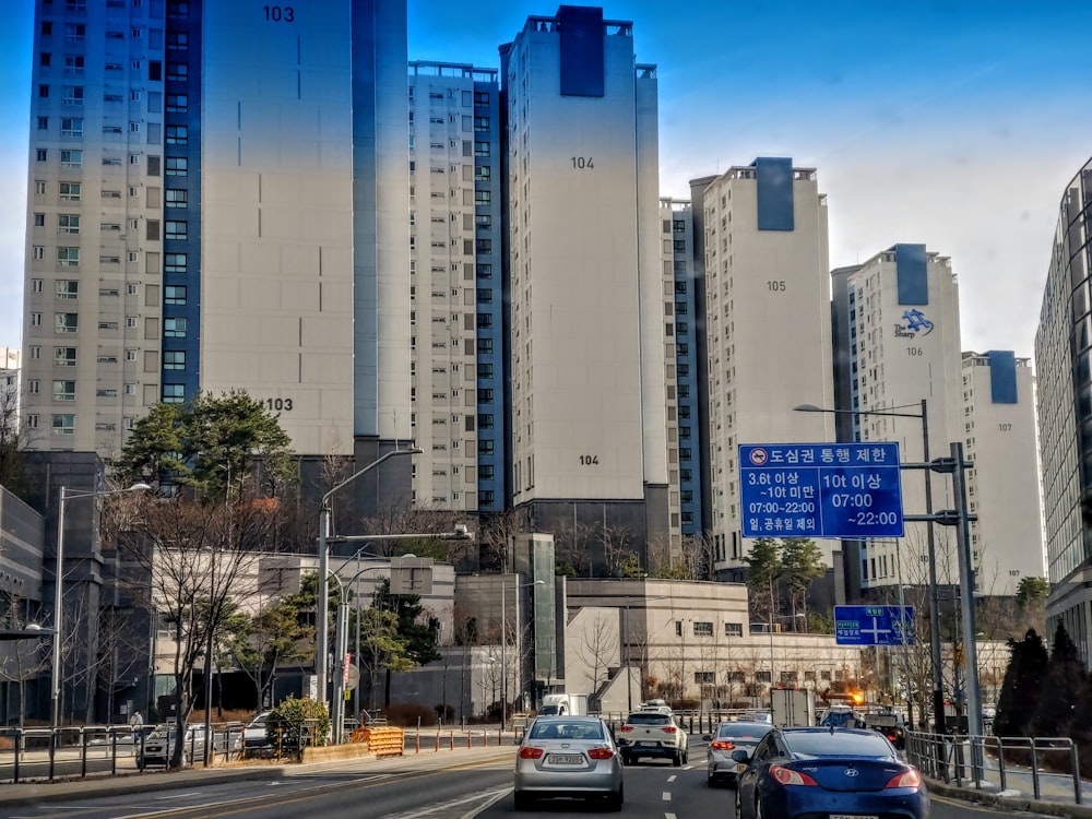 a group of cars driving down a street next to tall buildings