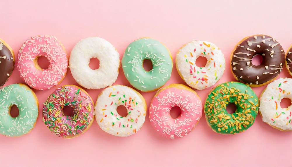 a row of doughnuts with different toppings on a pink background