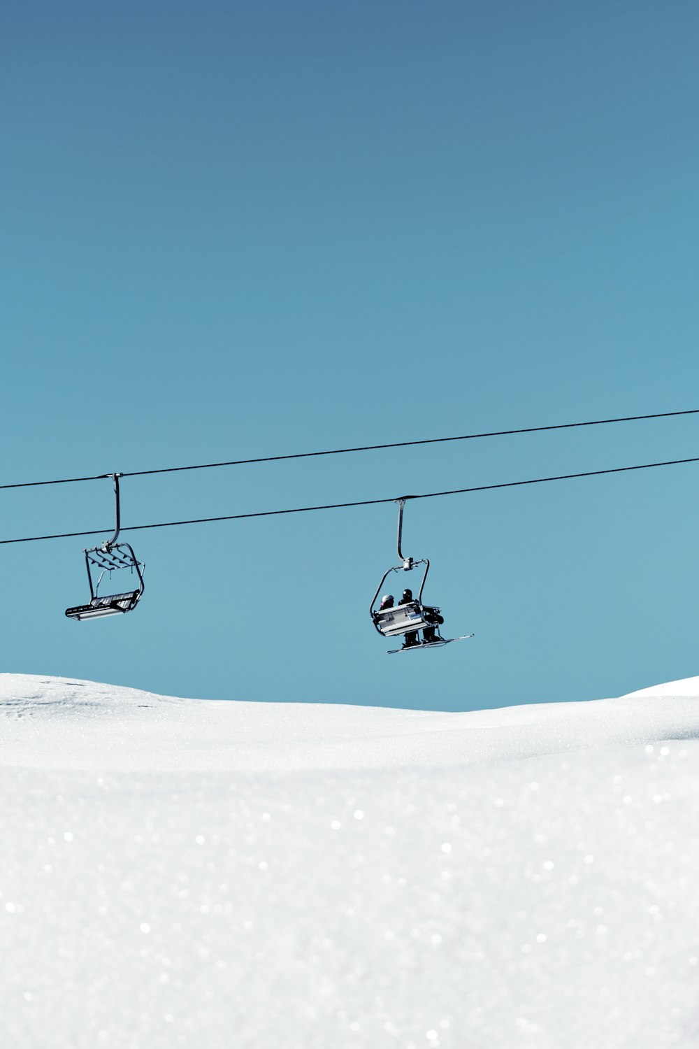 a ski lift with two skiers going up a snowy hill