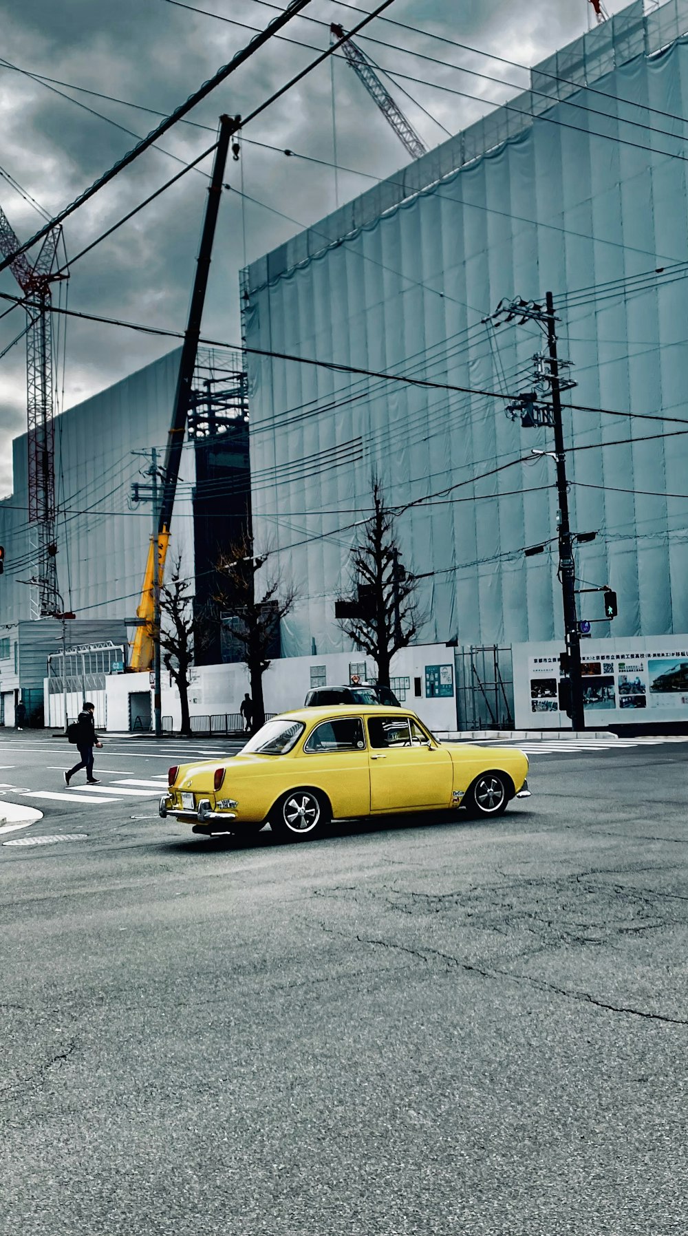 a yellow car driving down a street next to a tall building