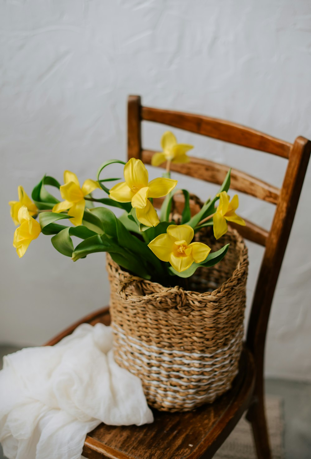 a basket of yellow flowers sitting on a wooden chair