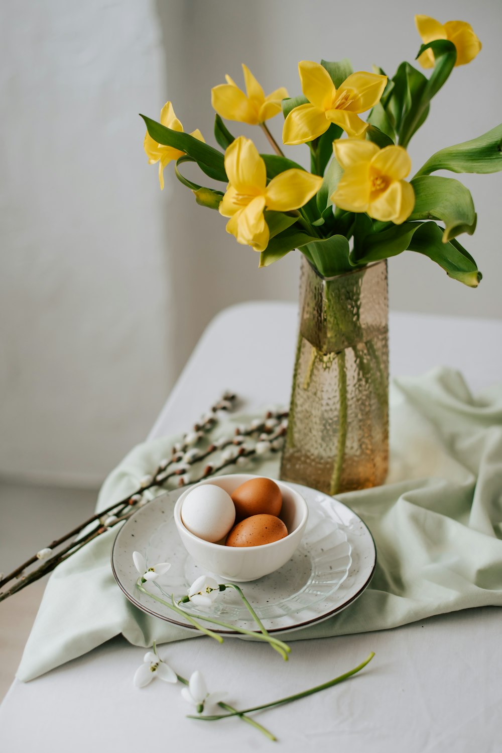 a glass vase filled with yellow flowers next to a bowl of eggs