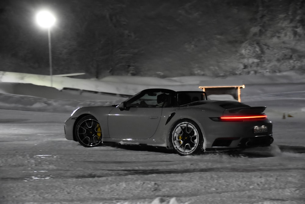 a grey sports car driving down a snow covered road