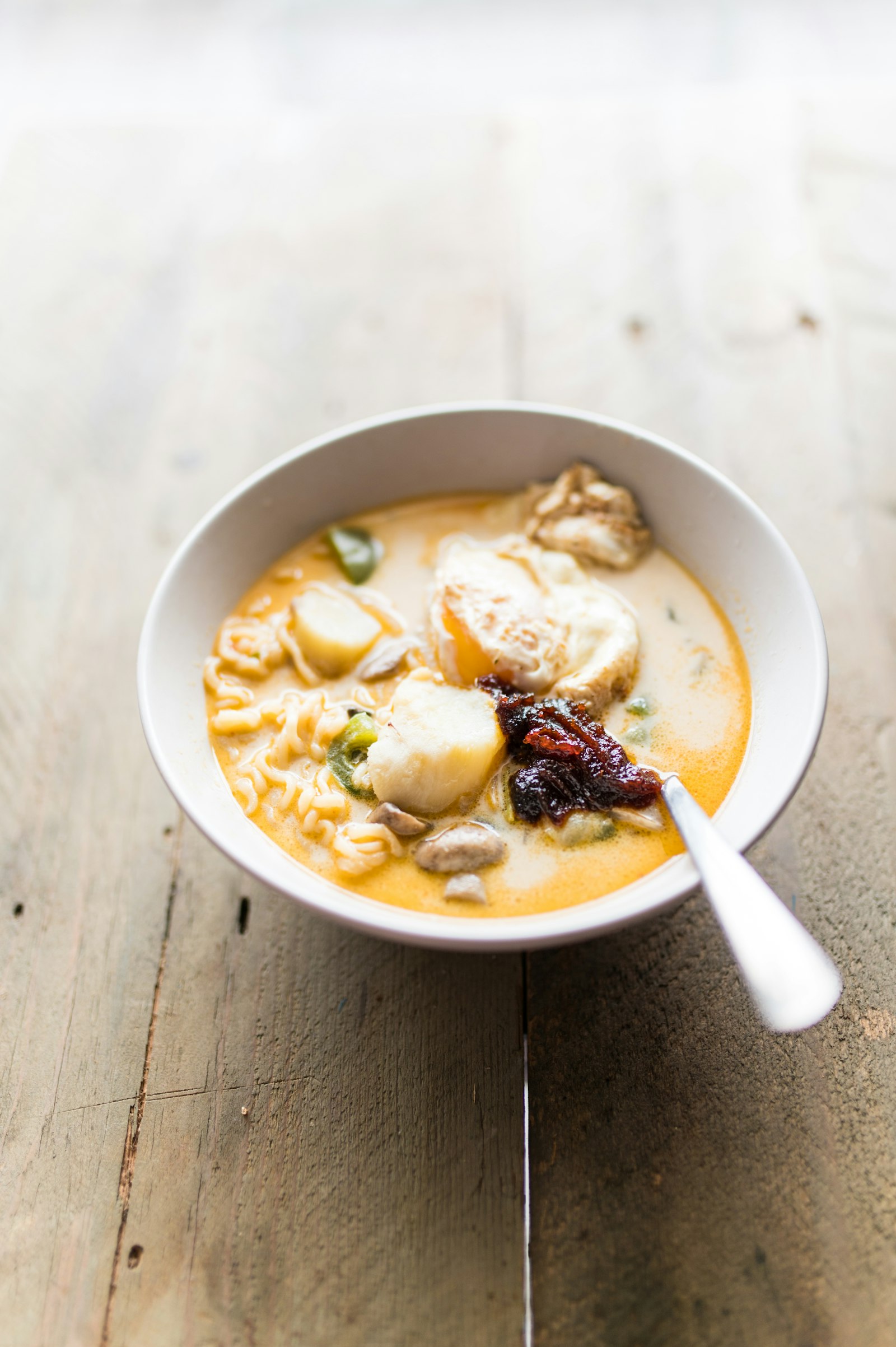 A bowl of laksa, a coconut-curry noodle soup with egg and sambal, on a wooden table