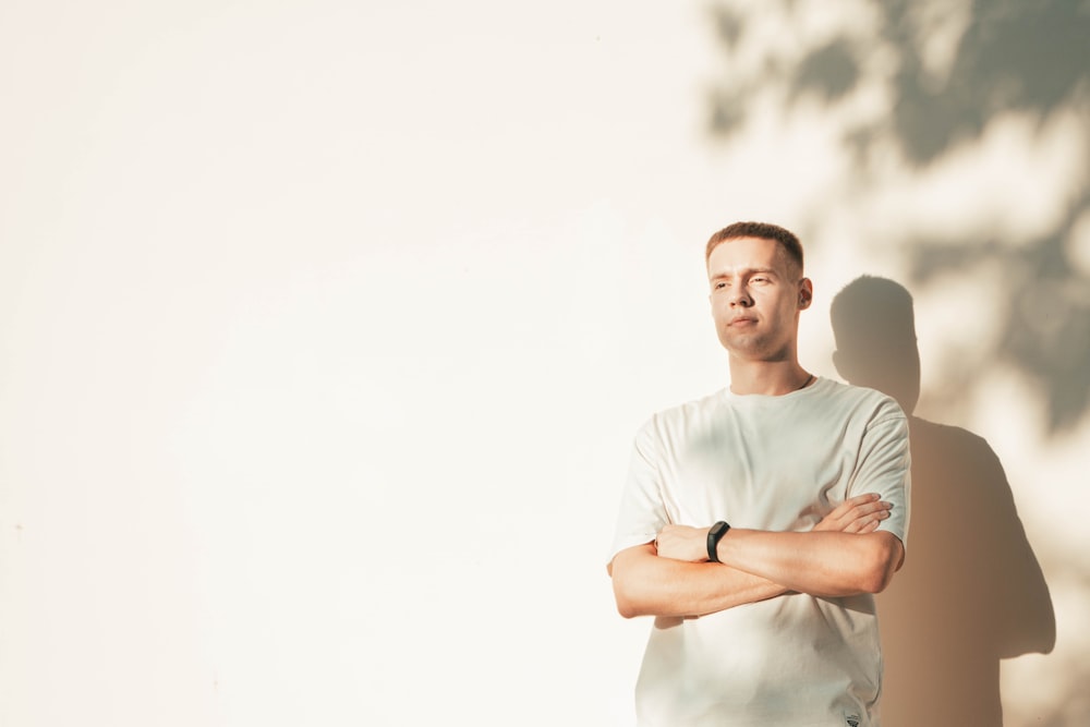 a man standing in front of a white wall with his arms crossed