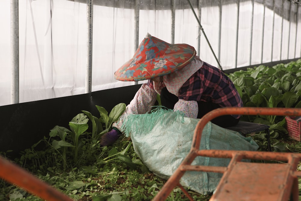 a woman kneeling down in a greenhouse with a hat on her head