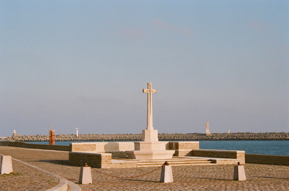 a cross sits on a stone bench next to a body of water