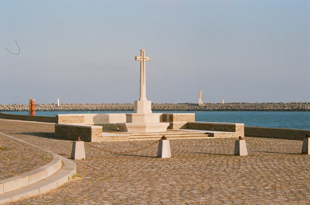a cross sits on a stone bench next to a body of water