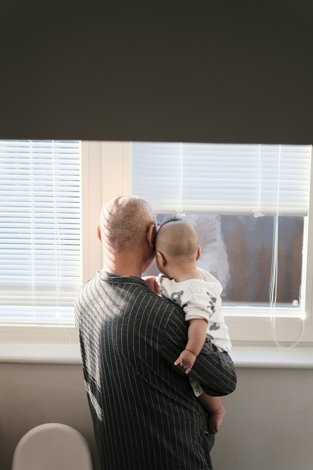 a man holding a baby in front of a window