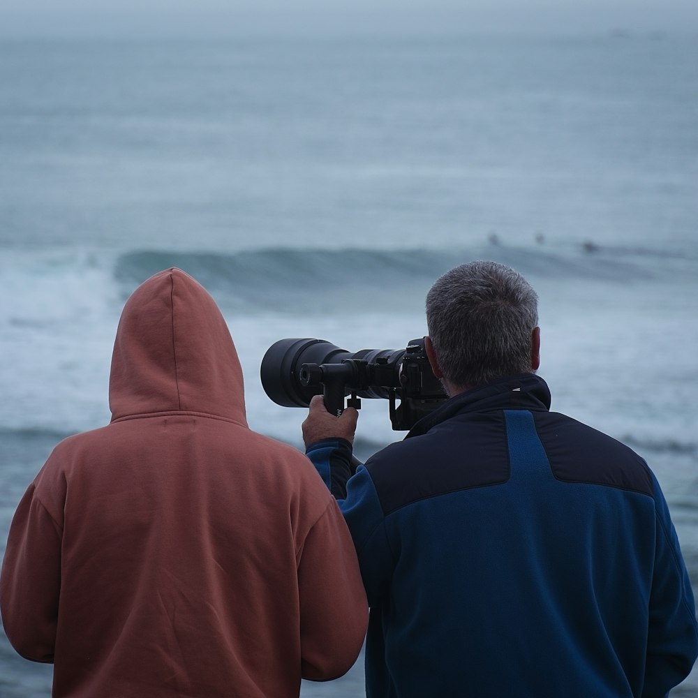 a man and a woman are looking at a wave with a camera