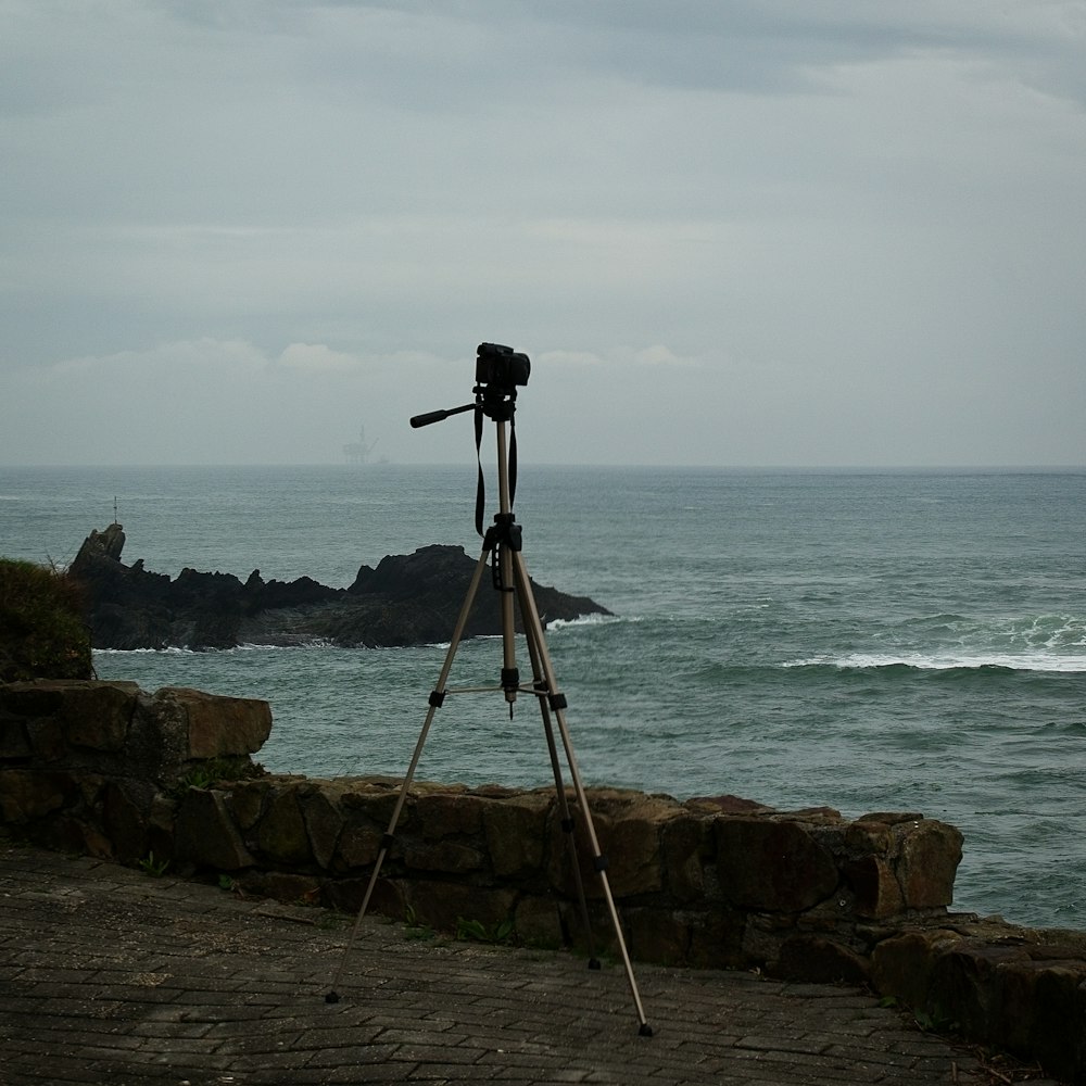 a tripod sitting on top of a stone wall next to the ocean