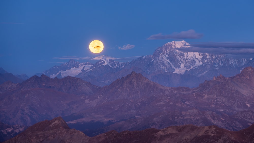 a full moon rising over a mountain range