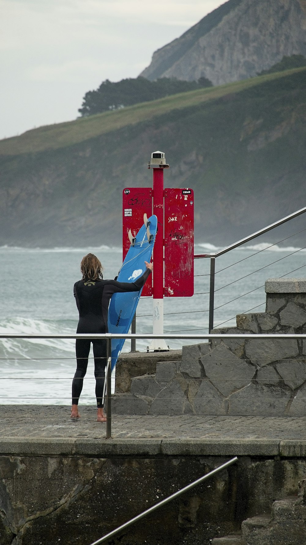 a woman holding a blue surfboard next to the ocean