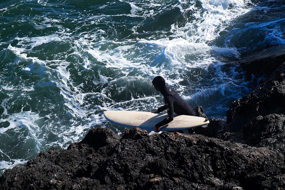 a person sitting on a rock with a surfboard