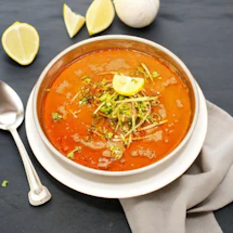a bowl of soup with a spoon and lemon wedges