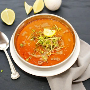 a bowl of soup with a spoon and lemon wedges