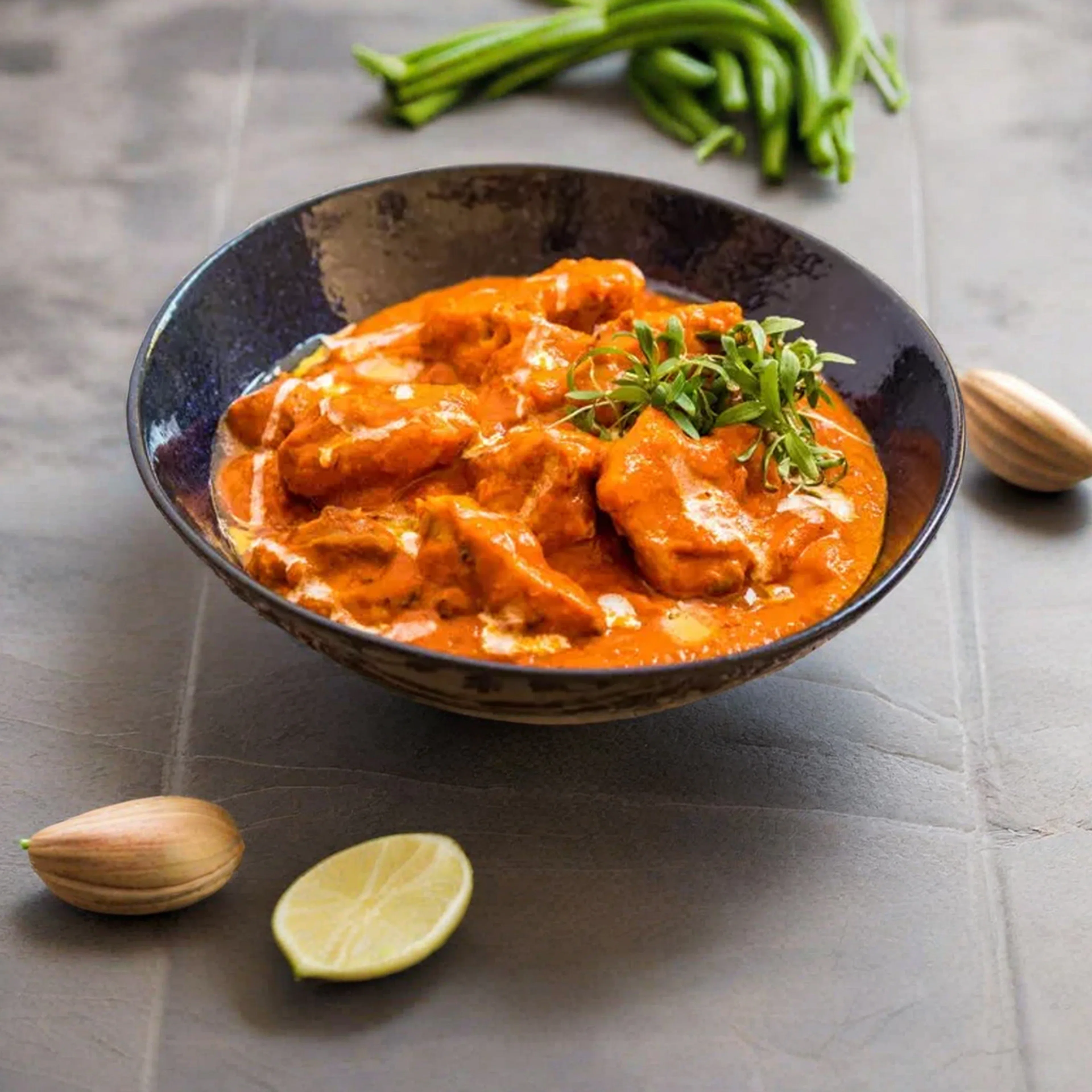 Dark bowl of butter chicken in a creamy orange tomato sauce with fresh herbs