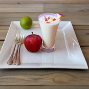 a white plate topped with a glass of milk and an apple