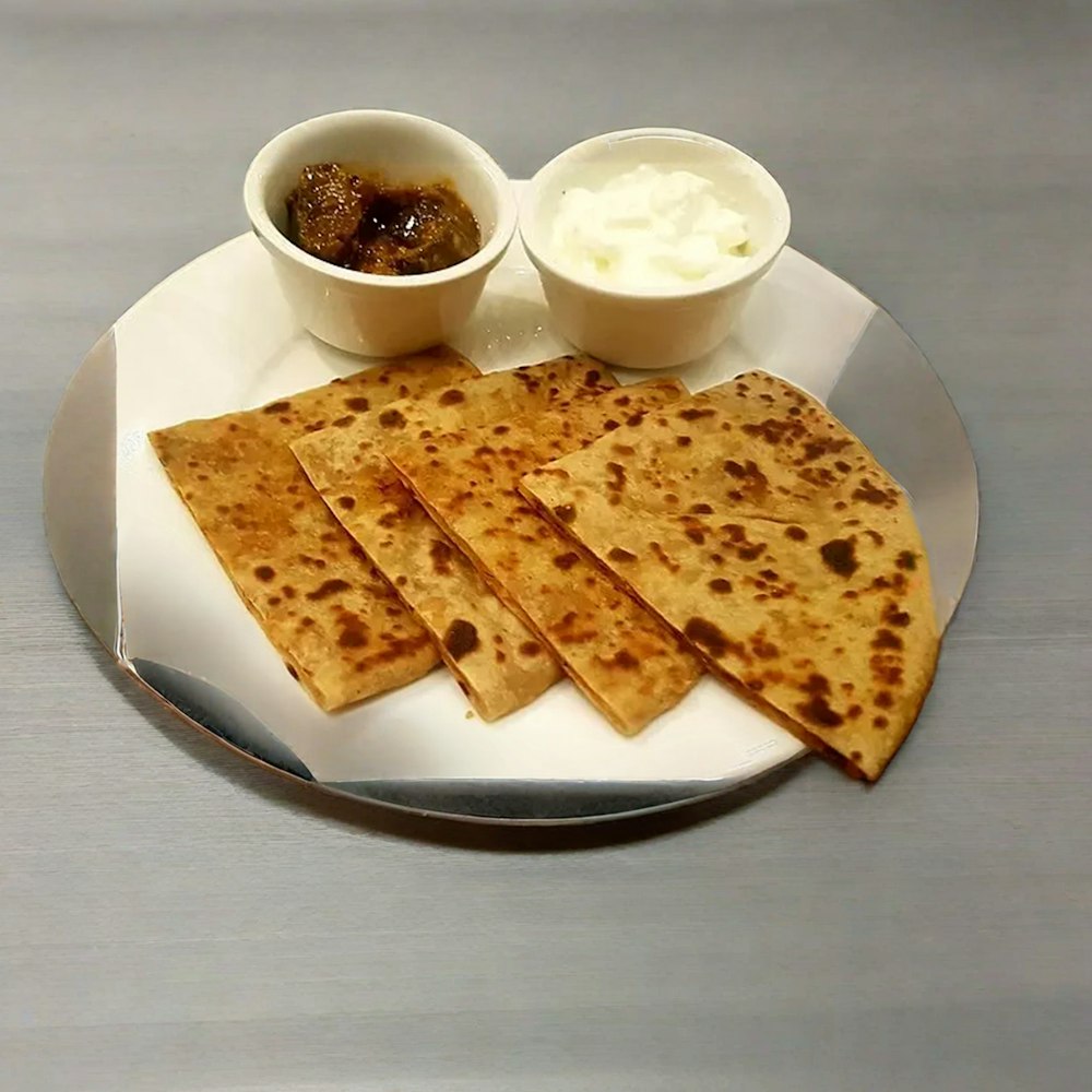 a white plate topped with flat bread next to a bowl of yogurt