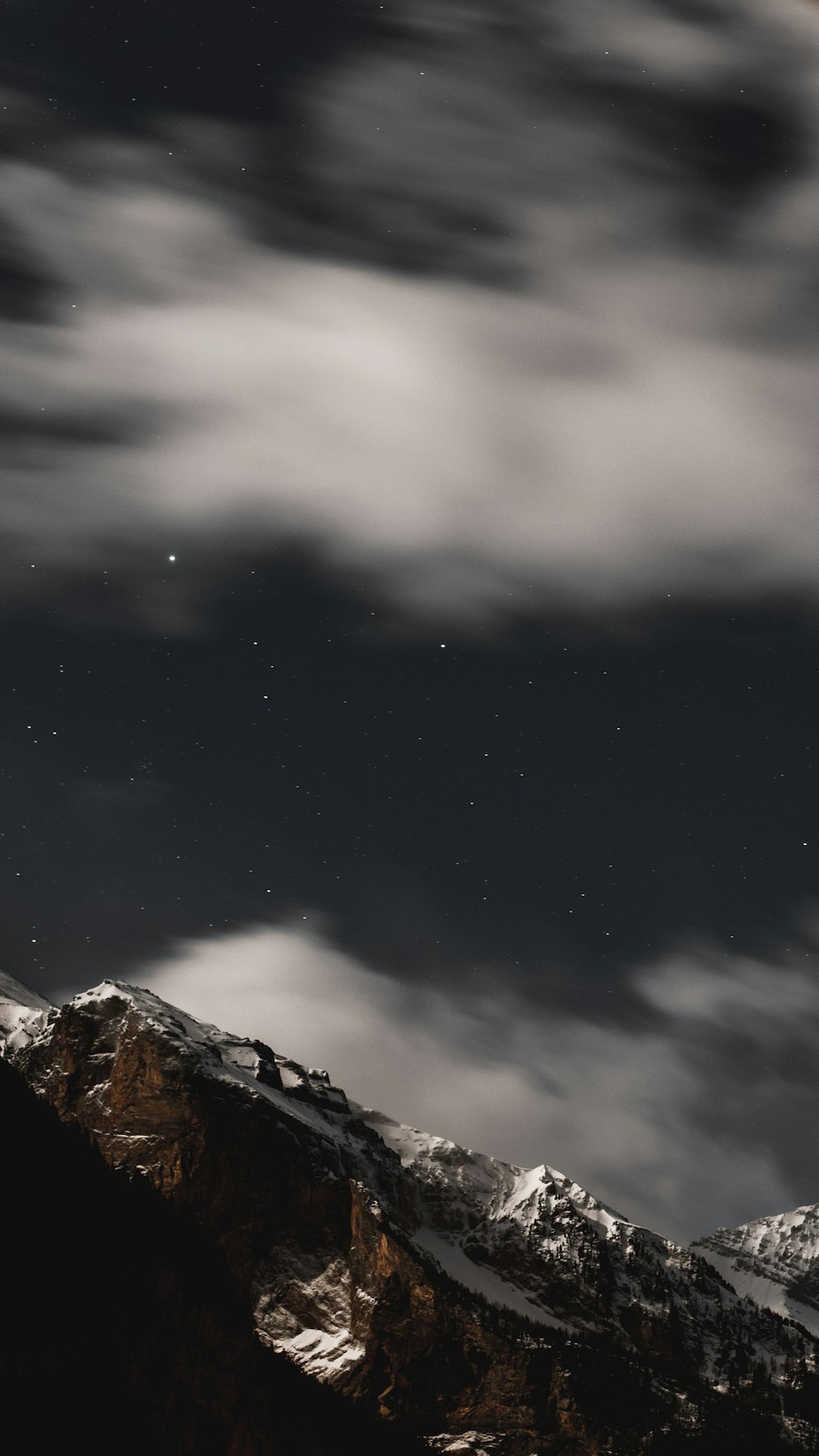 a night sky with stars and clouds over a mountain
